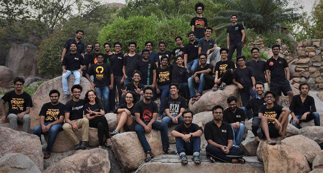 Group photograph of Crux members sittin on a rock formation.